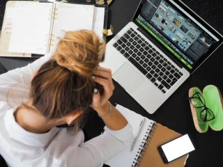 Vrouw zit voor een laptop met haar handen voor haar ogen