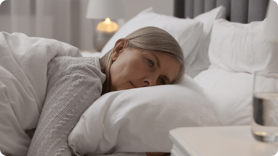 Vrouw van middelbare leeftijd kijkt ligt met hoofd op kussen, kijkt naar nachtkastje en kan niet slapen