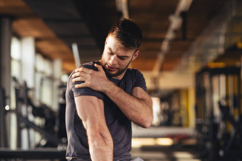 Man in de sportschool legt hand op schouder, een pijnlijk gewricht